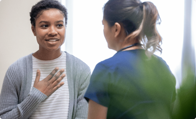 Smiling female patient touch chest while conversing with medical staff